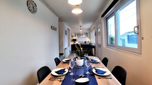 Un comedor con una larga mesa dispuesta para seis personas, sillas, un reloj en la pared y un ventanal con vistas al exterior.