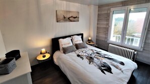 Un dormitorio moderno con una cama grande, dos mesitas de noche, una obra de arte en la pared y un ventanal con vistas.
