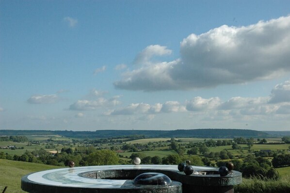 A circular stone structure with a clear view of a green landscape and distant hills.