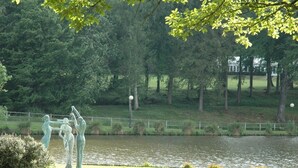 A park with a pond, a statue of three figures, and a grassy area with trees.