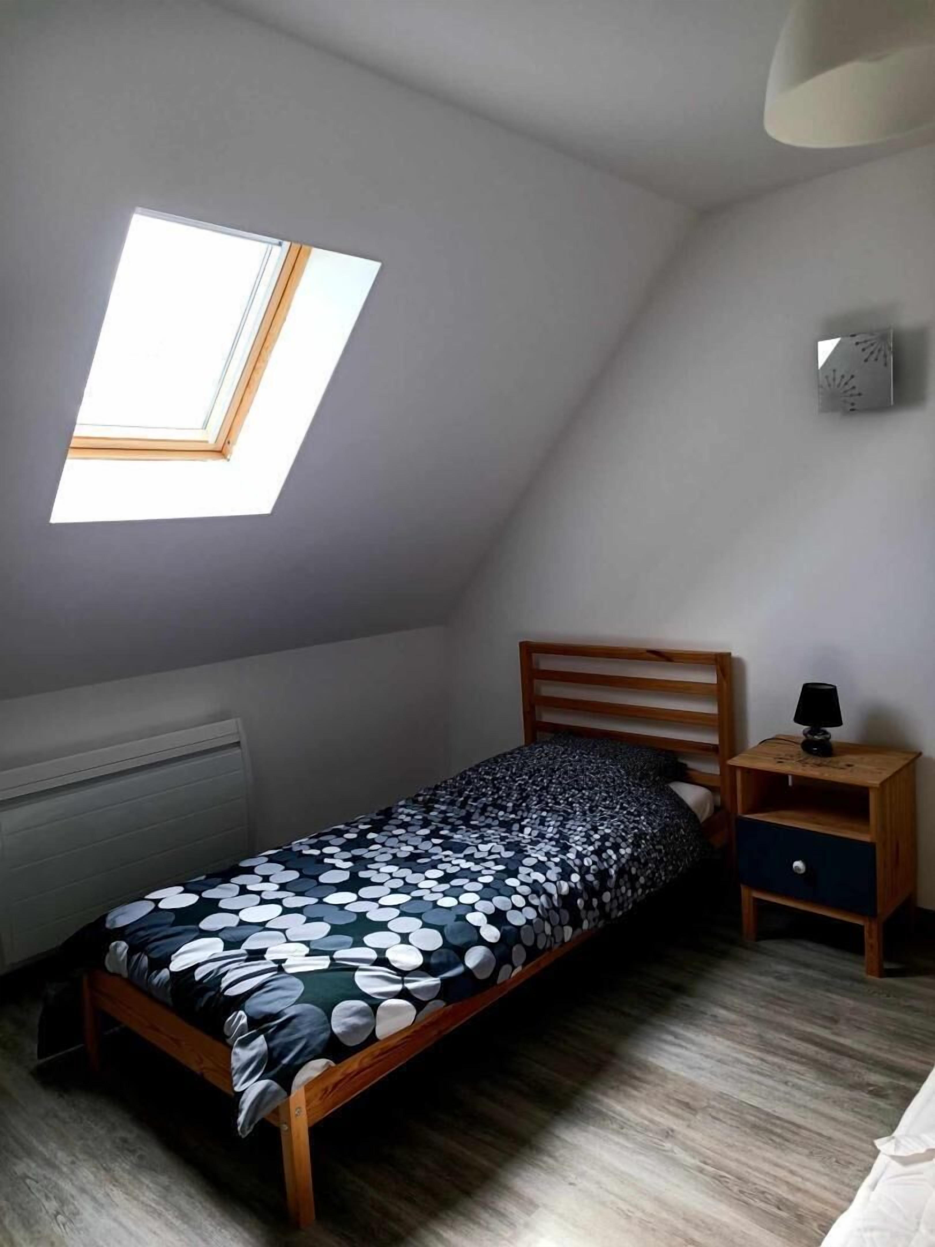 Una habitación pequeña con cama individual, techo inclinado y tragaluz.