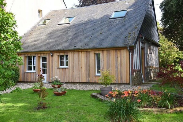 Une maison en bois avec un toit en pente, de nombreuses fenêtres et un jardin où poussent différentes plantes et fleurs.