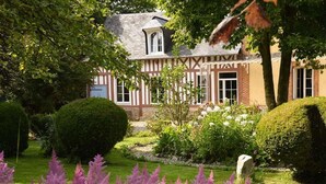A traditional half-timbered house with a well-maintained garden, including neatly trimmed hedges and flowering plants. - Gîtes de France® - The Cottage (BOUDEVILLE)