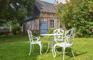 Une maison traditionnelle à colombages, avec un petit jardin et une table et des chaises en métal peintes en blanc.