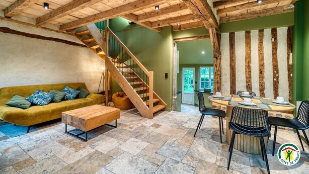 A spacious living area with a wooden staircase, a sofa, a coffee table, and a dining table with chairs. - Gîtes de France® - The Cottage (BOUDEVILLE)