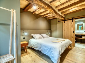 A bedroom with a wooden ceiling, a bed with white bedding, a bedside table, and a nightstand.