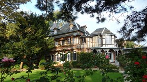 Una casa grande de dos pisos con un estilo arquitectónico tradicional, rodeada por un jardín bien cuidado con diversas plantas y flores.