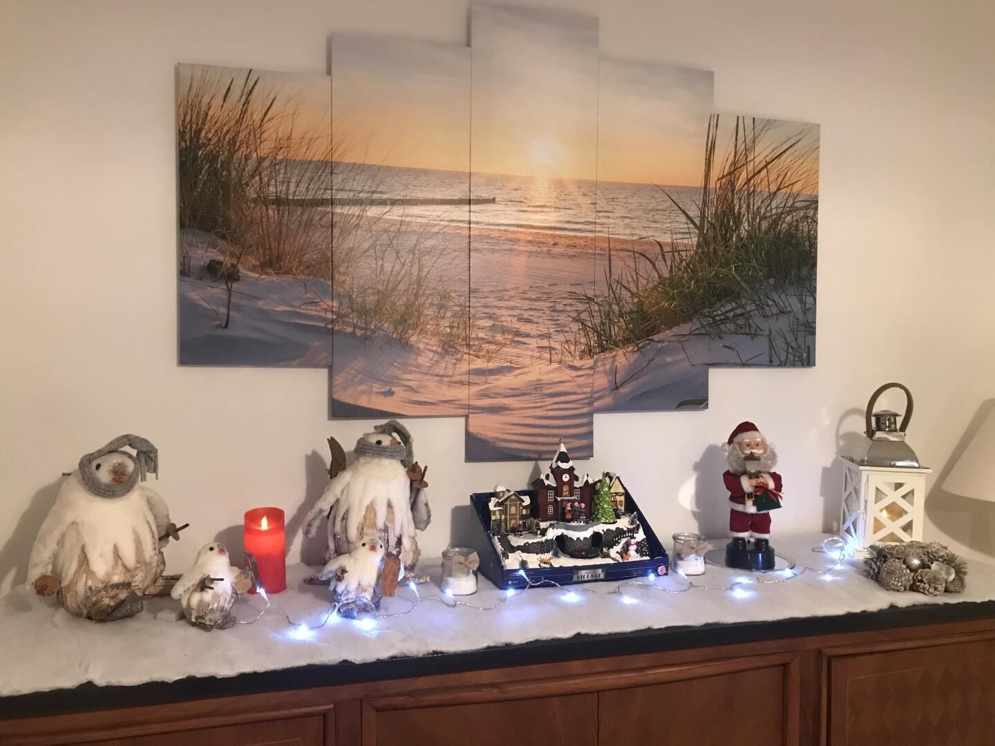 Una repisa decorada con una pintura de escena invernal, un figurito de muñeco de nieve, una vela, un pueblo en miniatura y una figura de Papá Noel.
