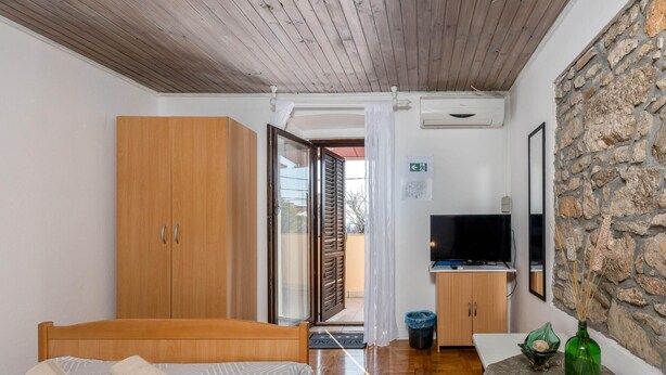 A compact room with a bed, a wooden wardrobe, a small kitchenette with a TV, and a stone wall. - Cozy apartment in Jadranovo with WiFi (Jadranovo)
