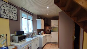 A kitchen with white cabinets, a microwave, a sink, and a large clock on the wall. - Gîtes de France® - Le Four à Chaux (CRIEL SUR MER)