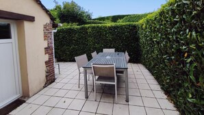 A patio with a table and chairs, a tiled floor, and a hedge. - Gîtes de France® - Le Four à Chaux (CRIEL SUR MER)