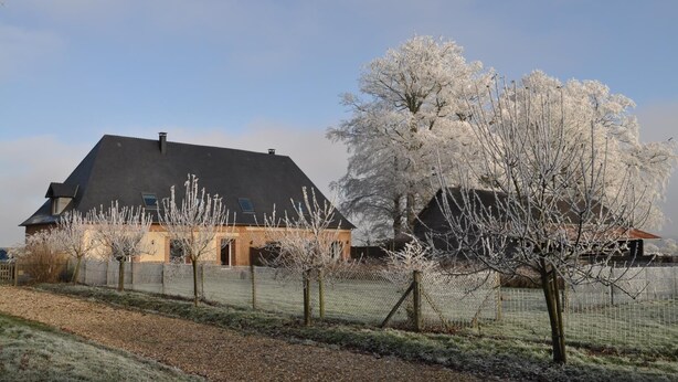 A house with a dark roof, a brick section, and a fenced yard with frost-covered trees. - Gîtes de France® - Le Neuf-Moulin (SAINT CRESPIN)