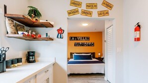 A hotel room with a bed, a coffee machine, and a shelf with various items.
