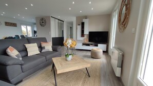 Un salon moderne avec un canapé gris, une table basse en bois et un téléviseur posé sur un meuble blanc.