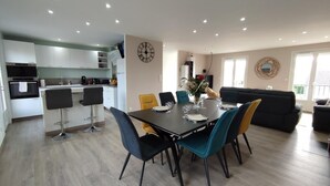 Une cuisine moderne avec des meubles blancs et un coin repas comprenant une table noire et des chaises turquoise.