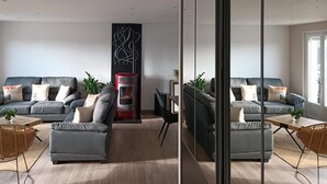 Un salon moderne avec deux canapés gris, une cheminée rouge et argentée, et un grand miroir qui reflète la pièce.