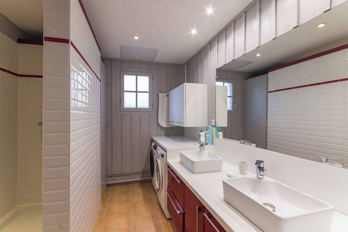 A modern bathroom with a large mirror, two sinks, a toilet, and a washing machine.