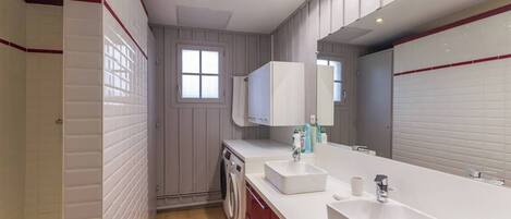A modern bathroom with a large mirror, two sinks, a toilet, and a washing machine.