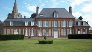 Un edificio grande e histórico con una torre destacada, ventanas simétricas y un césped bien cuidado.