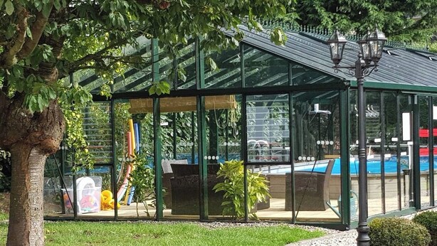 Un invernadero con techo de vidrio, piscina y césped bien cuidado.
