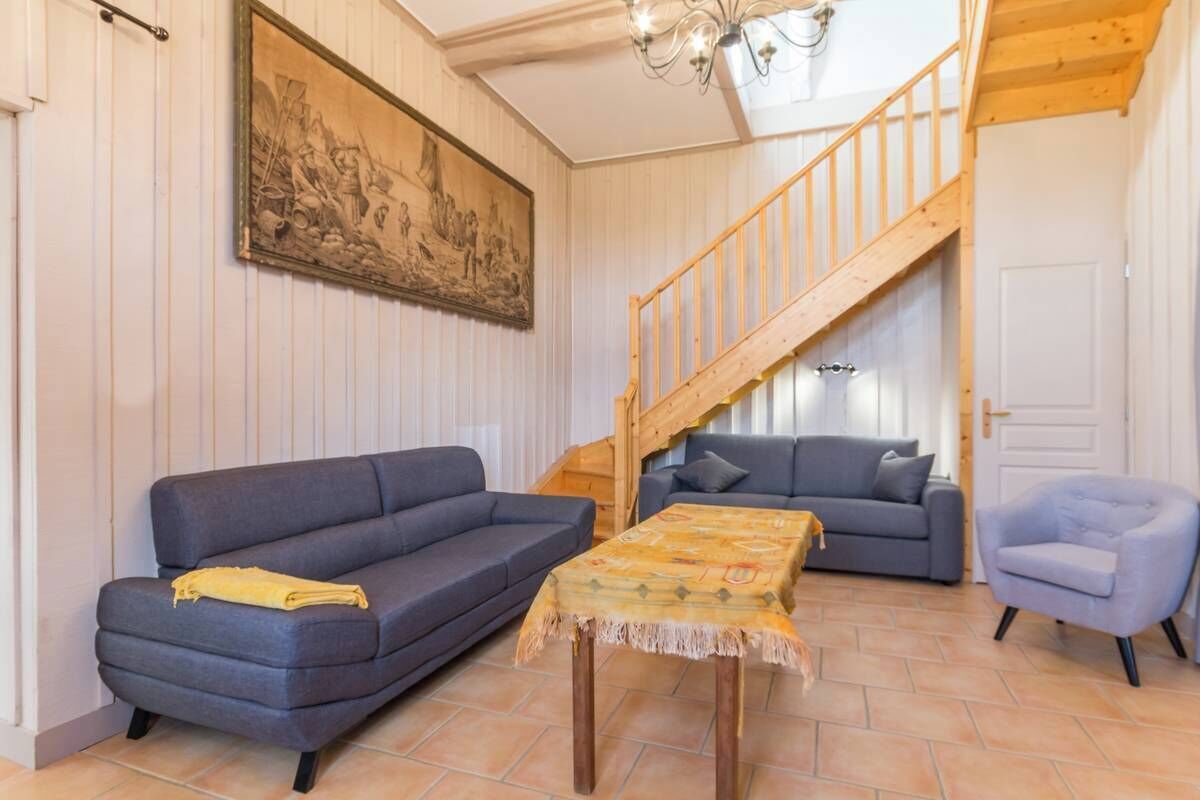 En stue med sofa, et lille bord, en stol, en trappe og et maleri på væggen.