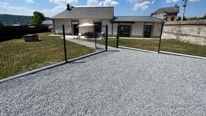 A building with a gravel driveway, a fenced area, and a stone wall.