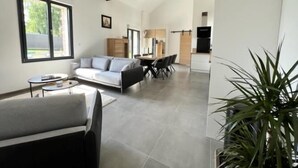 A spacious living area with a modern sofa, a dining table, and a kitchen in the background.
