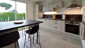 Une cuisine moderne avec une grande table à manger, deux chaises, une machine à café et un four.