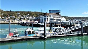 Un port de plaisance situé au bord de l’eau, avec des bateaux amarrés, un pont piétonnier et un immeuble à plusieurs étages.