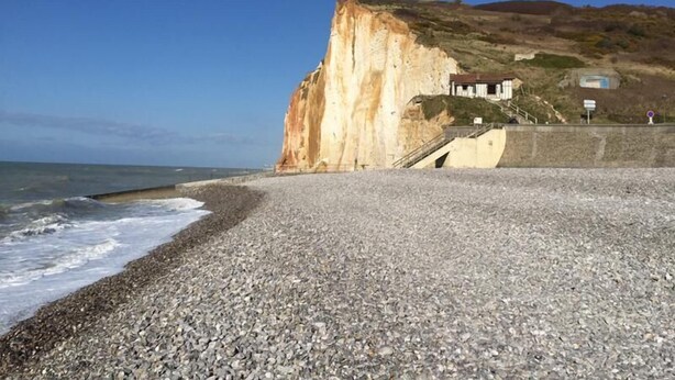 Une plage de galets, avec une grande falaise et un bâtiment situé sur la droite.