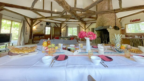 A dining area with a long table set for a meal, surrounded by wooden beams and a brick fireplace.