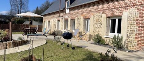 Una casa de ladrillo con un patio, mobiliario exterior y una parrilla.