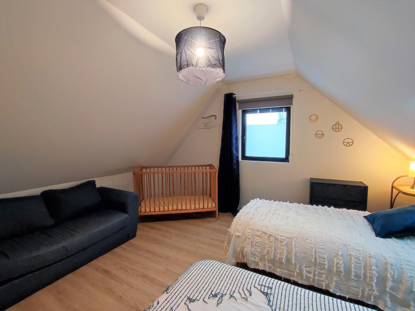 Una habitación pequeña y acogedora con techo inclinado, una cuna, un sofá y una cama.