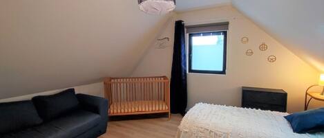 Una habitación pequeña y acogedora con techo inclinado, una cuna, un sofá y una cama.