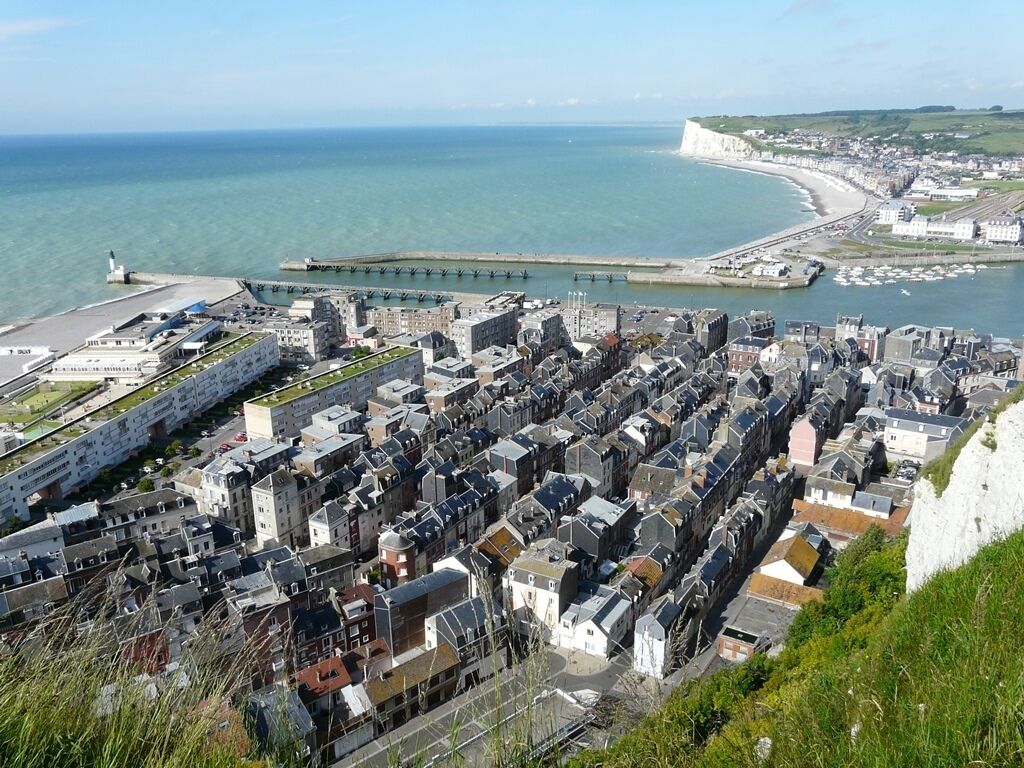Une ville côtière caractérisée par une concentration importante de bâtiments, une jetée qui s’avance dans la mer et une falaise blanche imposante en arrière-plan.
