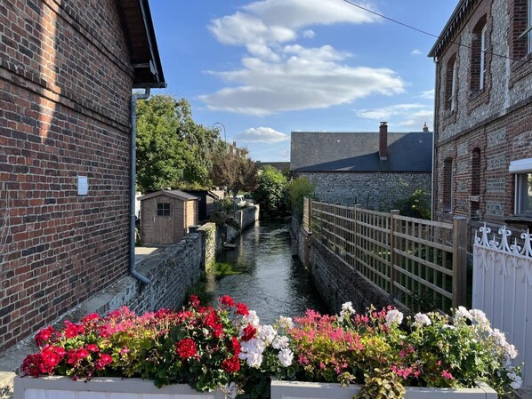 A narrow waterway flanked by brick buildings, with a wooden fence and flower beds in the foreground.