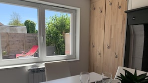 Spisestue med et bord dækket til to, et vindue der viser en rød stol udenfor, og et træskab med knager.