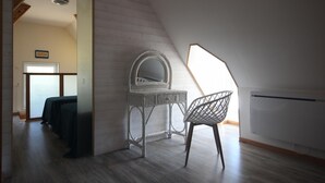 Et værelse med skråvægg, et hvidt fletskrivebord med et spejl, en moderne stol og udsigt gennem et stort vindue.