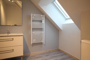 Une petite salle de bain moderne, dotée d’un puits de lumière, d’un radiateur blanc et d’un design minimaliste.