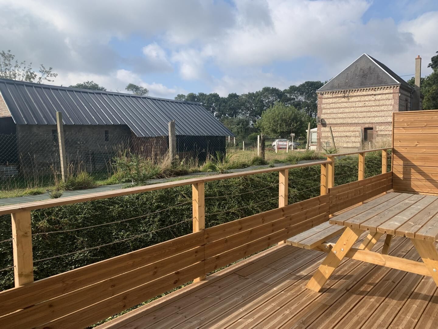 A wooden deck with a metal fence, a brick building, and a metal-roofed structure.