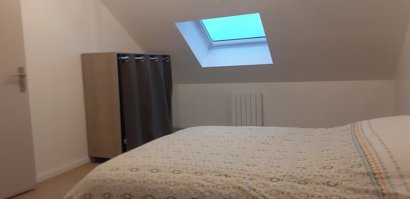 Une chambre avec un puits de lumière, un radiateur et un lit recouvert d’une couvre-lit à motifs.