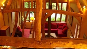 Un interno rustico con travi a vista in legno, un'accogliente zona salotto e ampie finestre che lasciano entrare luce naturale.