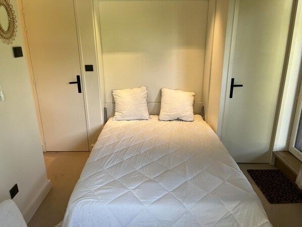 A bedroom with a bed, two pillows, a door, and a window.