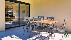 An outdoor patio with a wooden table and metal chairs, a glass door leading to a garden, and a logo on the wall. - Gîtes de France® - In the heart of Senneville (SENNEVILLE SUR FECAMP)