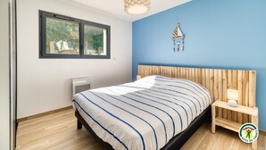 A bedroom with a bed, a nightstand, a wall-mounted lamp, a window, and a ceiling light fixture. - Gîtes de France® - In the heart of Senneville (SENNEVILLE SUR FECAMP)