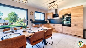A modern kitchen with wooden cabinets, a dining area with a table set for four, and a large window offering a view of the outdoors. - Gîtes de France® - In the heart of Senneville (SENNEVILLE SUR FECAMP)