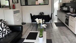 Une cuisine moderne avec des meubles blancs, un coin repas avec une table et des chaises noires, et un salon avec un canapé noir et une table basse.