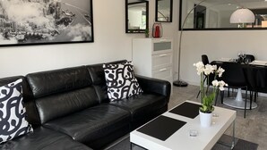 Un salon moderne avec un canapé en cuir noir, une table basse blanche et un tableau représentant un paysage urbain accroché au mur.
