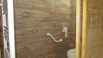 Een badkamer met houten vloer, een wit toilet, een handgreep en een handdoekdispenser.