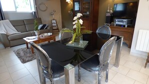 A dining area with a black table and clear chairs, a sofa, a coffee table, and a TV in the background.